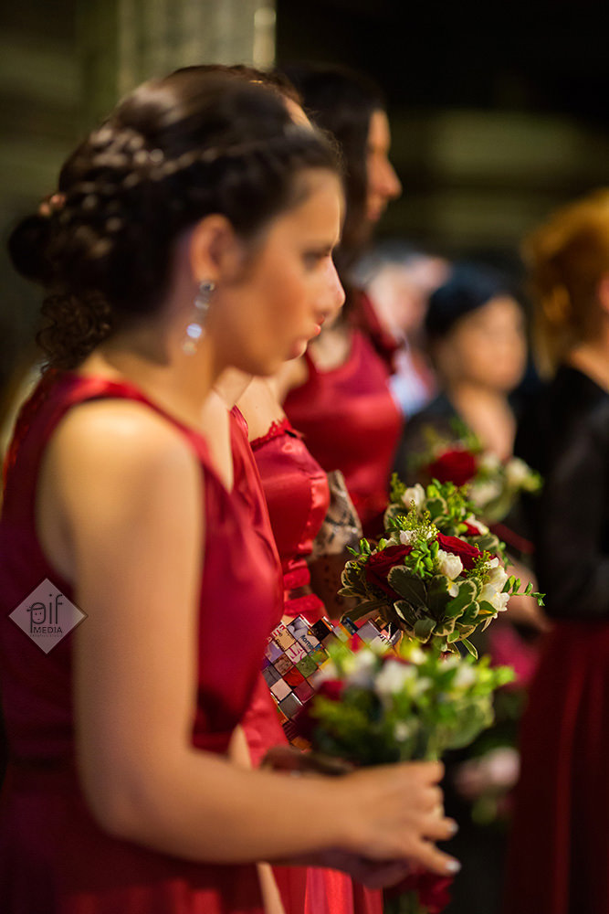 domnisoare cu rochii rosii si buchete de flori cu verde in biserica la cununia religioasa